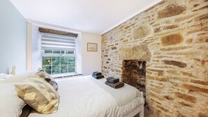 Ein Schlafzimmer mit einer Steinsäule, einem Bett mit weißer Bettdecke und einem Fenster mit Jalousien.