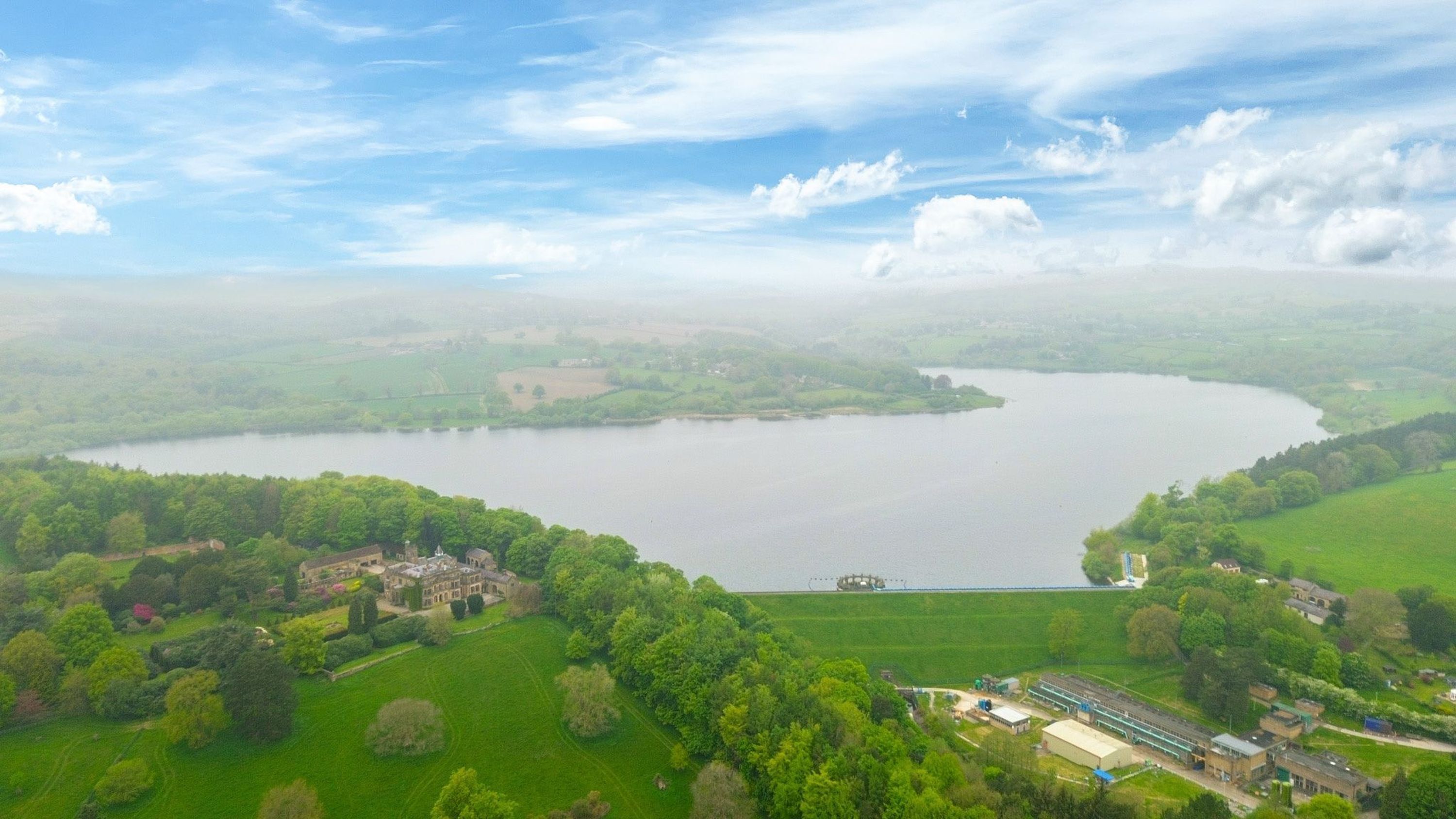 Un grand lac entouré de vastes prairies verdoyantes et un bâtiment historique doté d’une tour.