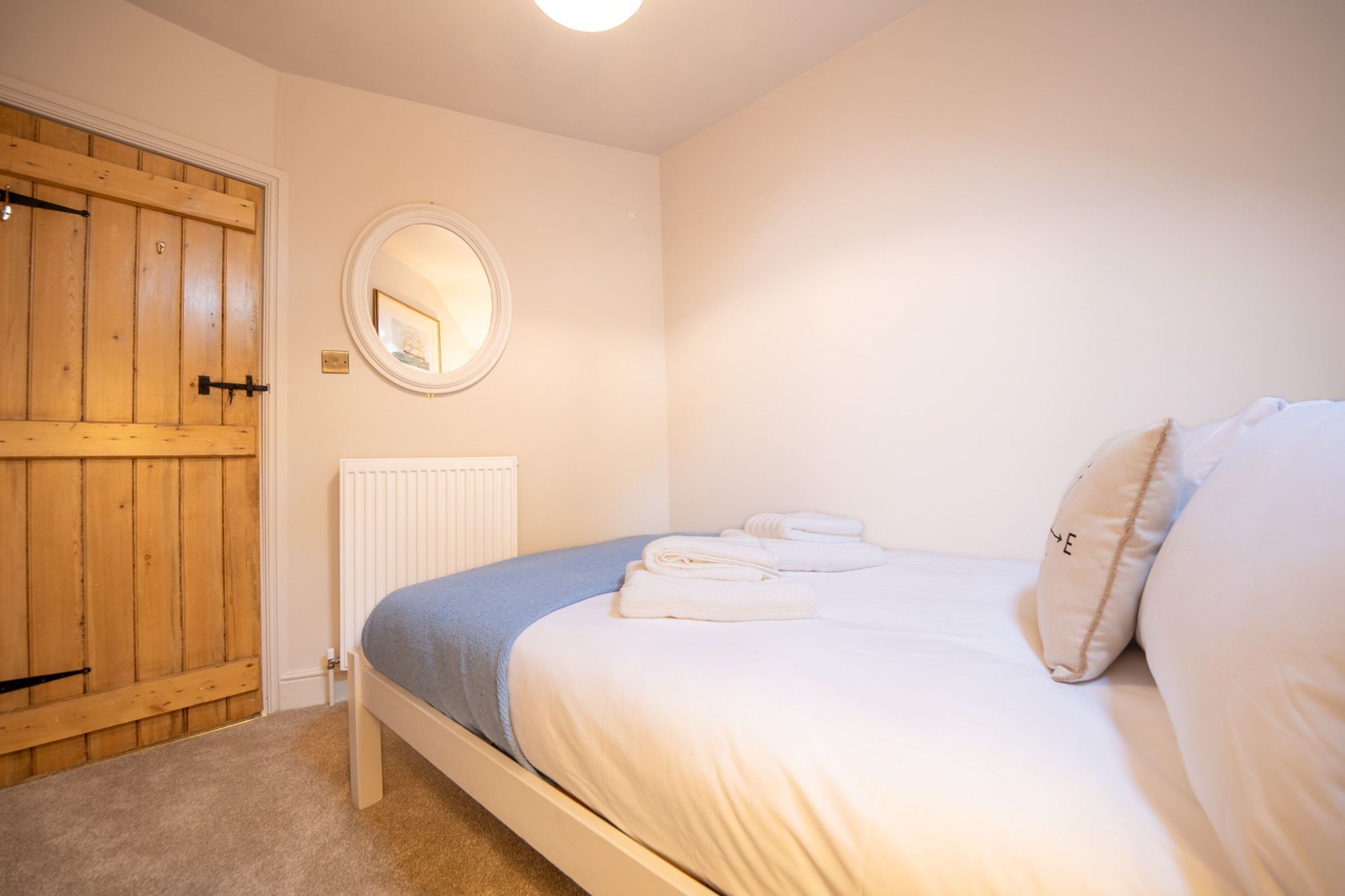A bedroom with a bed, a wooden door, a white radiator, and a round mirror on the wall.