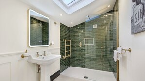 Een moderne badkamer met dakraam, een vrijstaand wastafelmeubel, een douche met glazen wanden en een betegelde wand.
