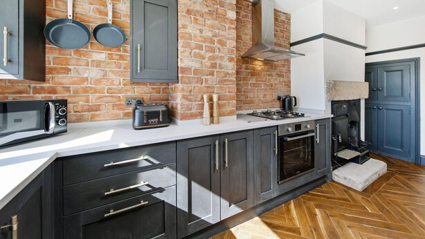 Een keuken met een bakstenen muur, moderne apparatuur en donkere kastjes.