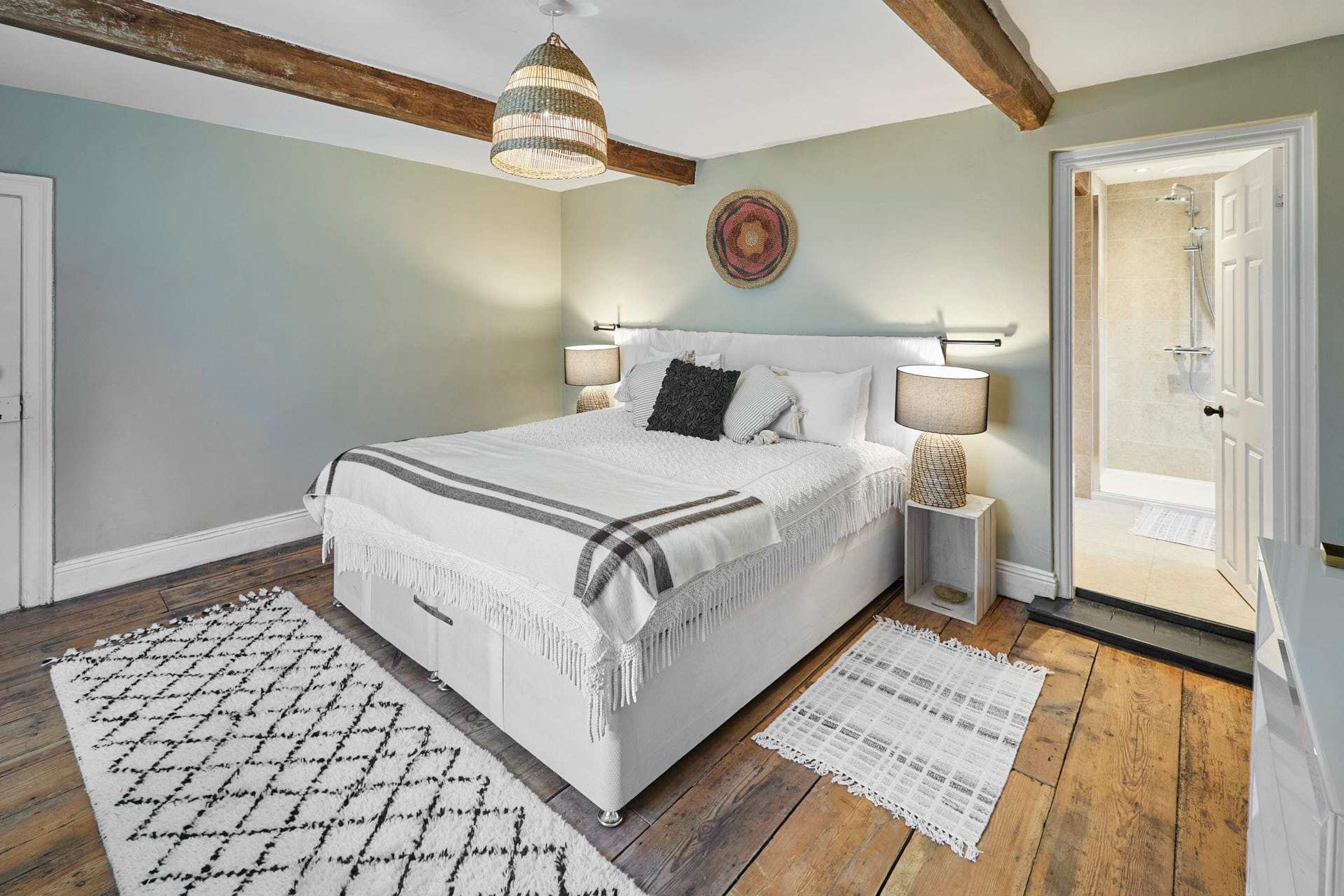 Ein Schlafzimmer mit einem großen Bett, Nachttischlampen, Holzboden und einer Tür zu einem Badezimmer.