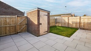 Un jardin avec un abri en briques, une clôture en bois et une terrasse dallée.