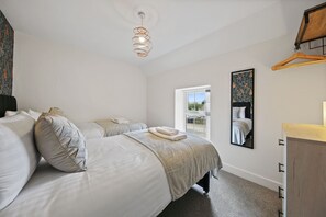 A bedroom with two beds, a hanging light fixture, a window, and a mirror. - Host Stay The Staffordshire Knot (Buxton)