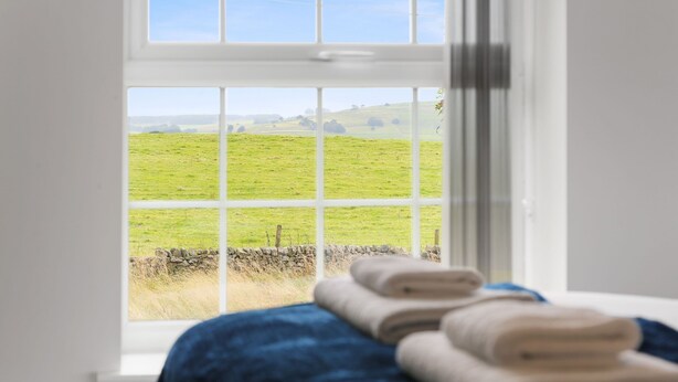 Ein Zimmer mit einem großen Fenster und Blick auf ein grünes Feld und eine Steinmauer.
