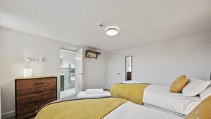 Ein Hotelzimmer mit zwei Betten, einem hölzernen Schminktisch, einem Spiegel und einem durchgegangenen Türspalte sichtbaren Badezimmer.