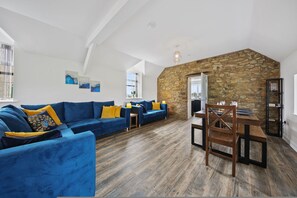 A modern living room with a blue sofa set, a dining table with chairs, and a stone accent wall. - Host Stay The Staffordshire Knot (Buxton)