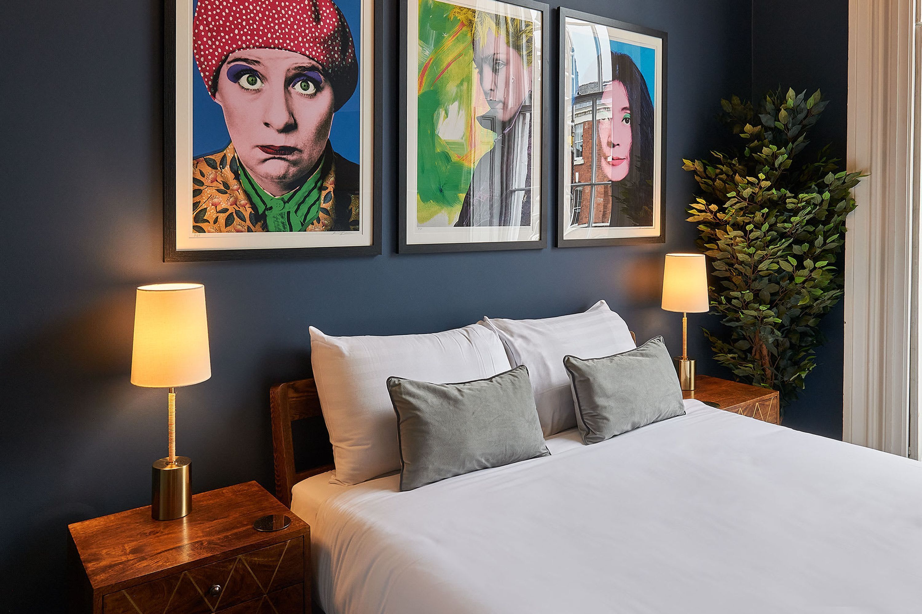 A neatly made bed with two pillows, two bedside lamps, and three framed artworks on the wall.