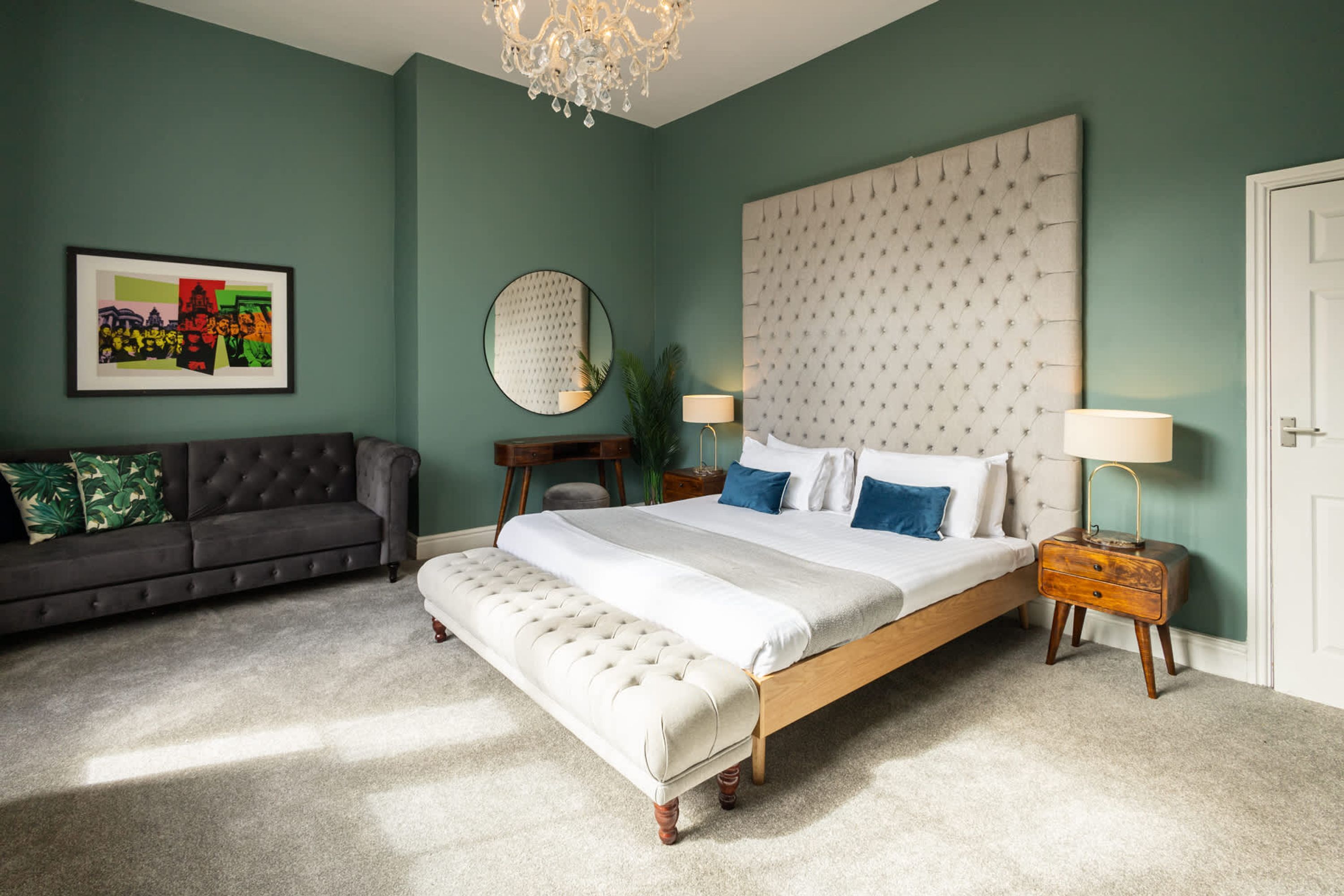 A bedroom with a large bed, a sofa, a chandelier, and a framed picture on the wall.