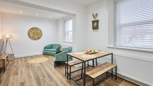 Ein Zimmer mit Holzboden, einem grünen Sofa, einem Tisch mit Obstschale, einer Wanduhr und einem Heizkörper.