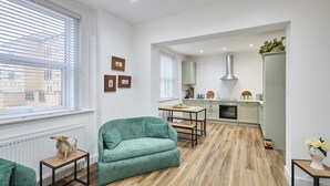 Ein modernes Wohnzimmer mit einem grünen Sofa, einem Esstisch und einer Küche im Hintergrund.