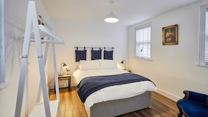 A bedroom with a bed, a ladder, a chair, a nightstand, a lamp, a window with blinds, and a framed picture on the wall. - Host Stay The Coach House Apartment 2 (Saltburn-by-the-Sea)