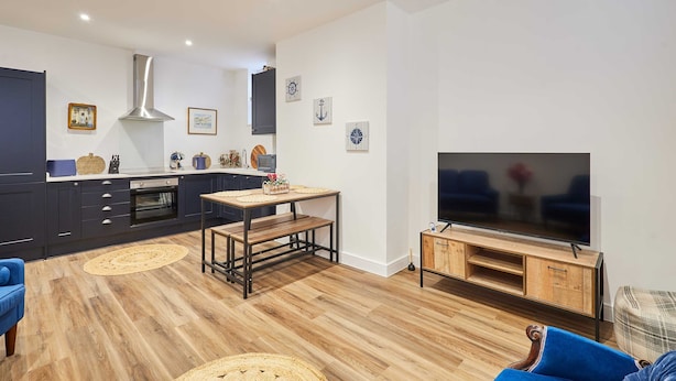 A modern kitchen with dark cabinets, a stainless steel range hood, and a wooden dining table. - Host Stay The Coach House Apartment 2 (Saltburn-by-the-Sea)