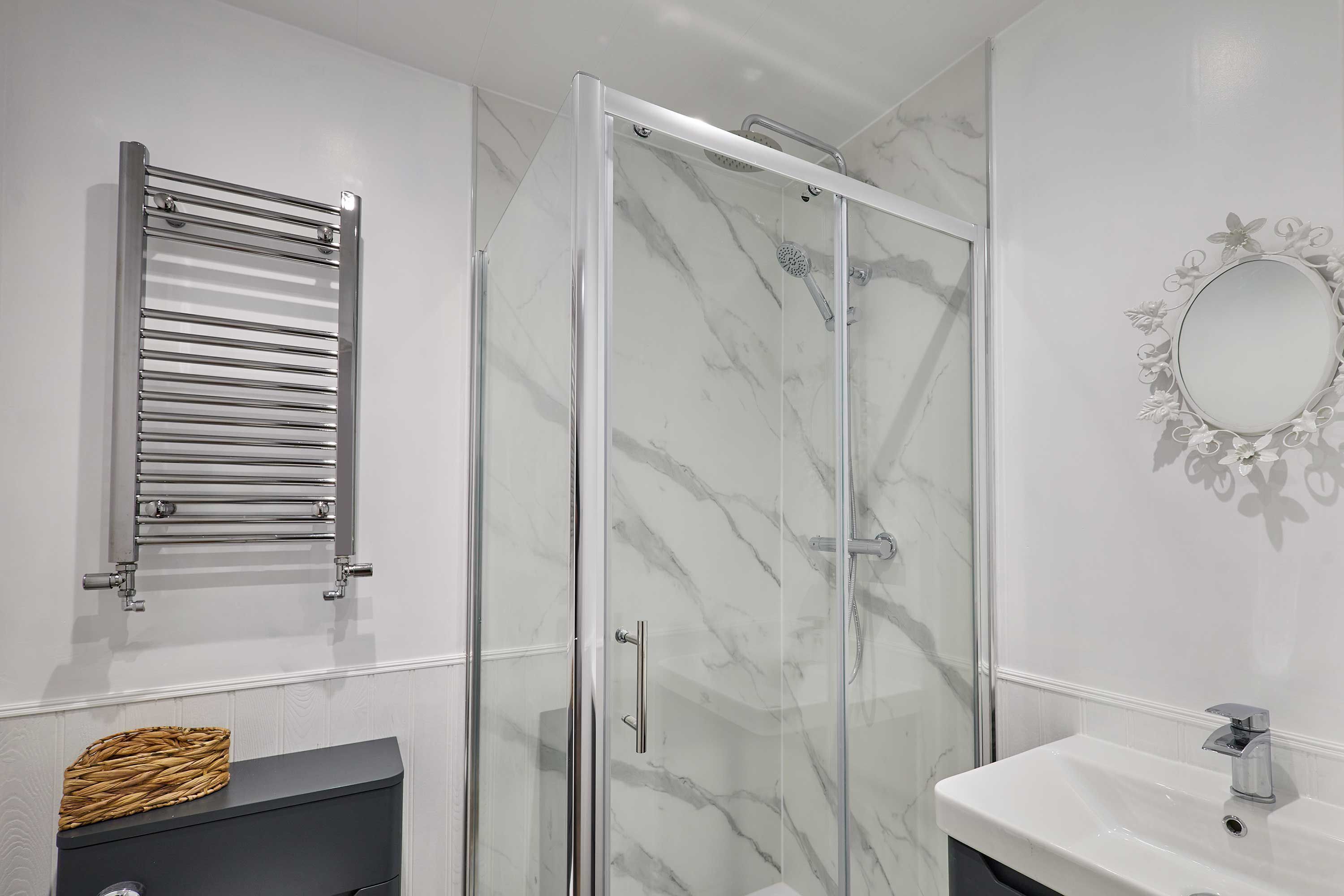A modern bathroom with a glass-enclosed shower, a white sink, and a towel rack.