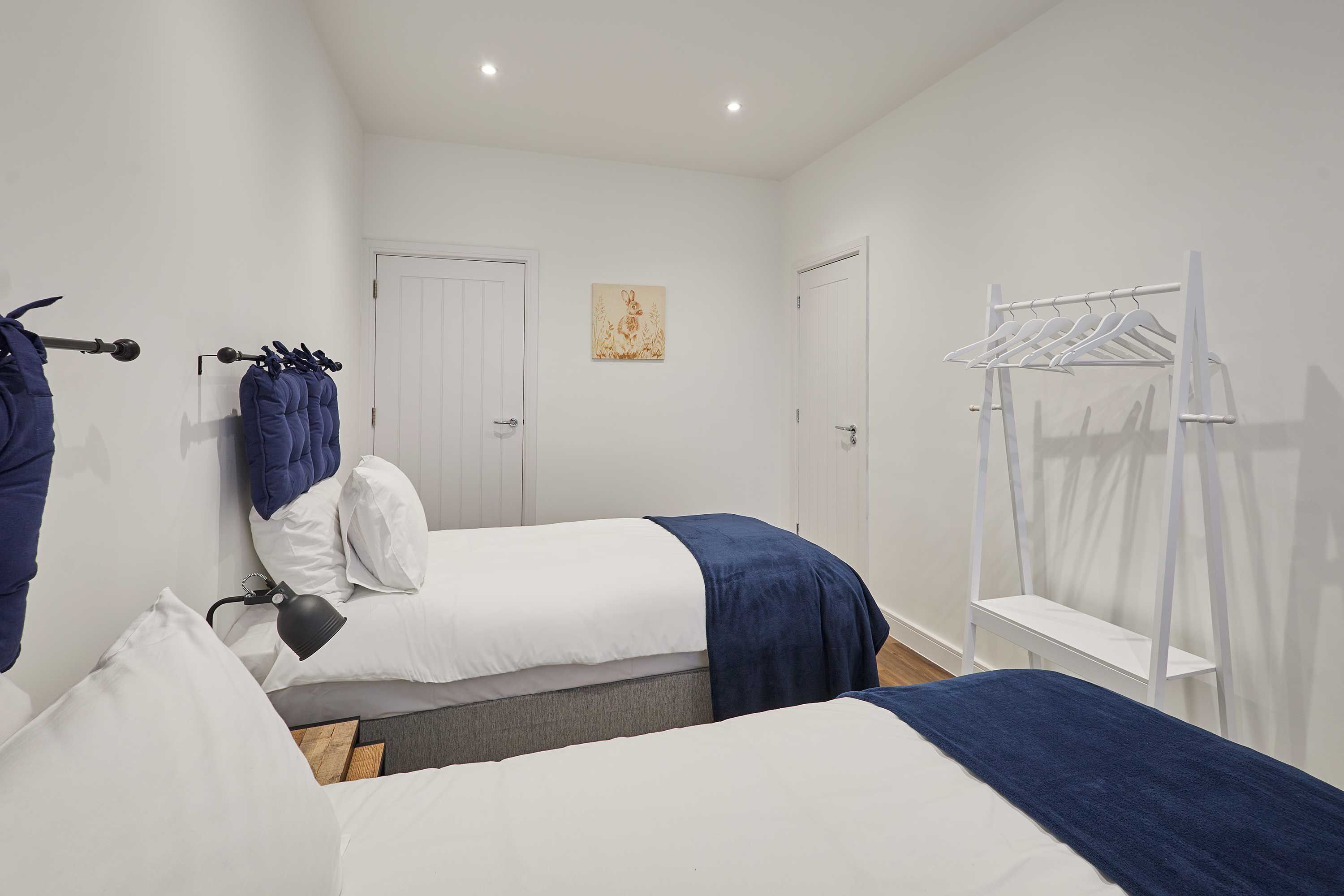 A bedroom with two beds, a white wardrobe, a white drying rack, and a wall-mounted lamp.