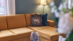 A tan sofa with patterned cushions, a floor lamp, and a glass of water on a table.