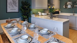 A modern kitchen with white cabinetry, a dining area set for six with a wooden table, and a framed map on the wall.