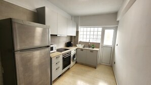 A compact kitchen with a stainless steel refrigerator, a microwave, a stove, and a washing machine.