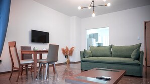 A modern living room with a flat-screen TV, a green sofa, a wooden coffee table, and a dining area with chairs and a table.