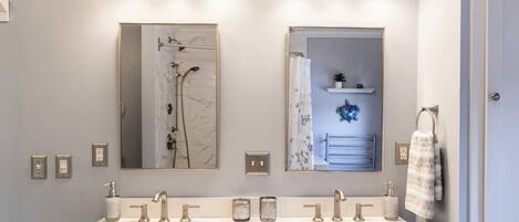 A bathroom with two sinks, a shower, and a mirror.