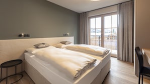 A hotel room with a large bed, a desk, and a view of the city through the window. - Amazing Apartment in Tyrol With Infrared Sauna (Westendorf)