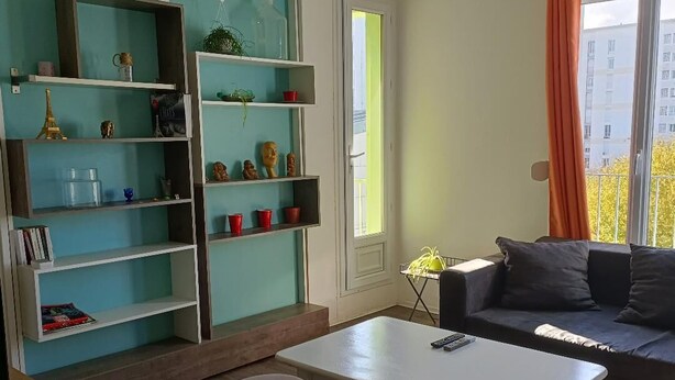 Una sala de estar con estanterías azul turquesa, un sofá, una mesa y dos taburetes.