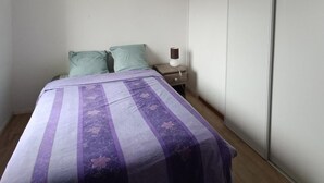 Un dormitorio pequeño con una cama, dos almohadas, una mesita de noche con una lámpara y una puerta de armario corredera.