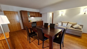 Ein Essbereich mit Holztisch und Stühlen, einer Couch und einer kleinen Küchenzeile im Hintergrund.