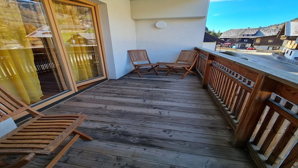 Eine Holzterrasse mit zwei Holzstühlen und einer Glastür, die zu einem überdachten Bereich führt.