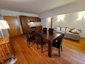 Un comedor con una mesa y sillas de madera, un sofá y una cocina al fondo.