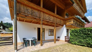 Una baita in legno con balcone, area salotto esterna e un giardino curato.