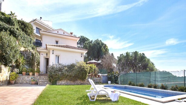 Una casa con piscina, prato e muro in pietra.