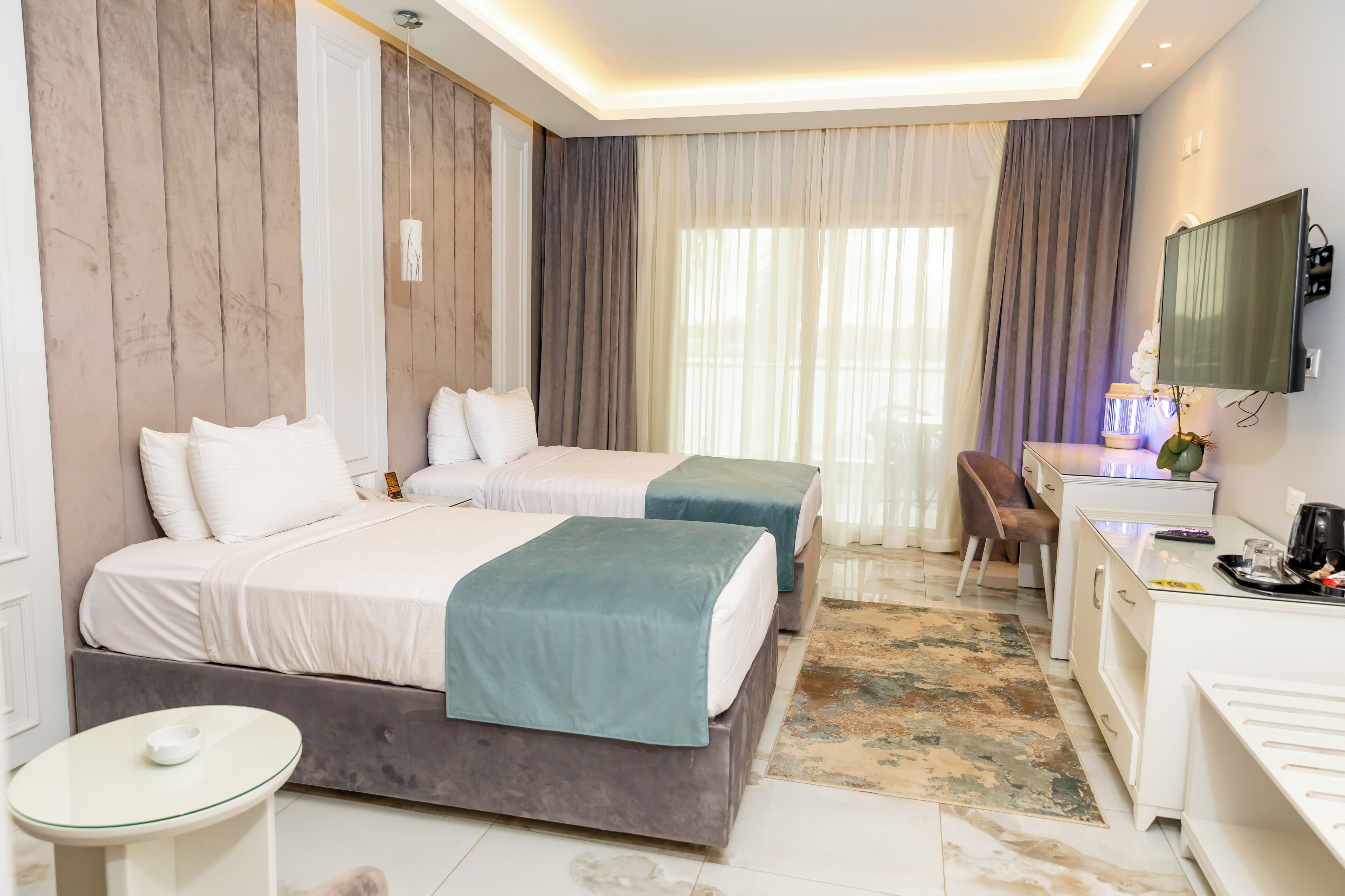 A modern hotel room with two beds, a desk, and a television.