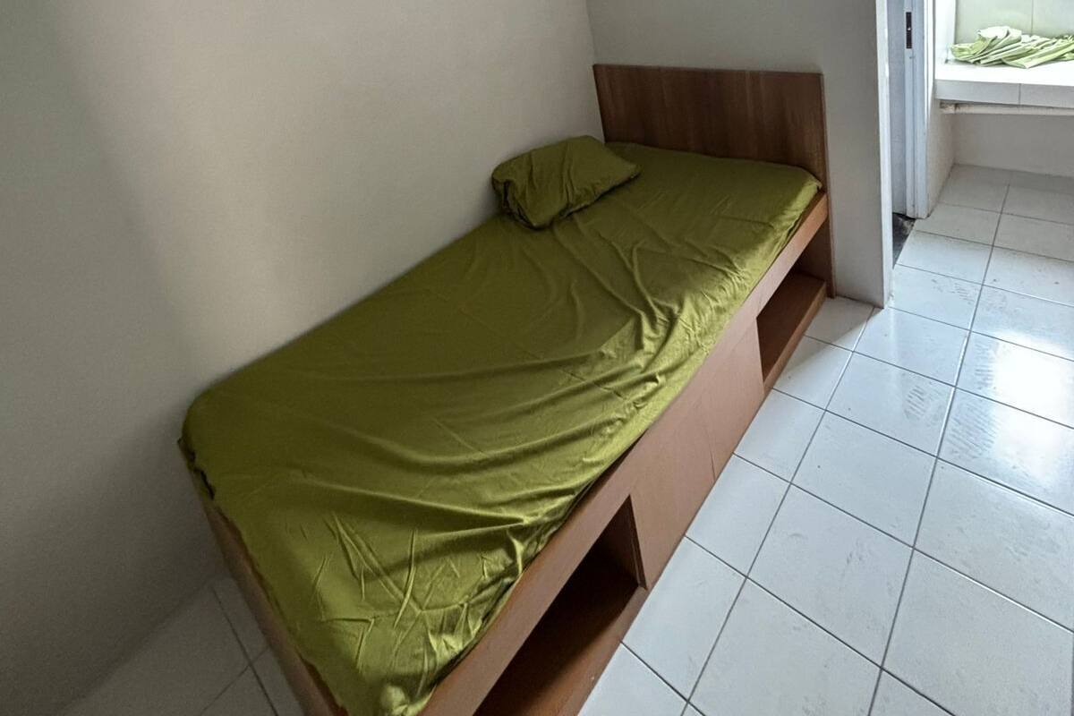 Een kleine kamer met een enkel bed, een houten frame, een groene matras en een vloer van witte tegels.