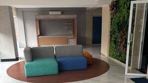 Un moderno vestíbulo con piso de mármol, un mostrador de recepción de madera, un conjunto de sofás y una pared verde con plantas.