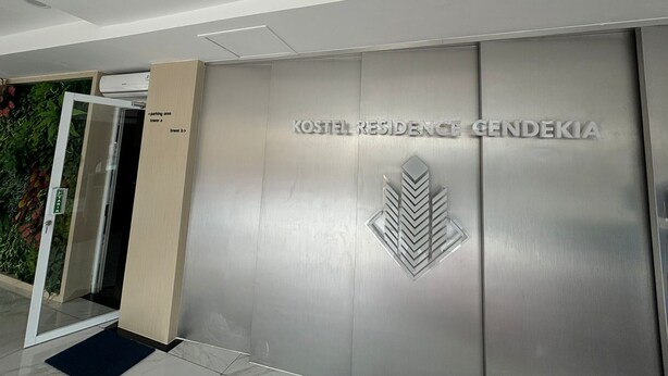 Una entrada moderna a un edificio con fachada metálica y un logo que dice "KOSTEL RESIDENCE GENDEKIA".
