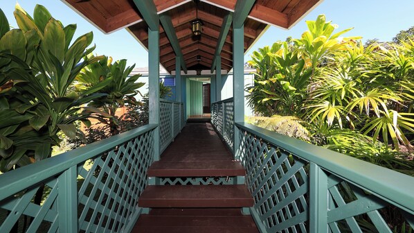 A covered walkway with a wooden ceiling and lattice railings, surrounded by lush tropical plants.