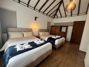 Une chambre d’hôtel avec deux lits, des têtes de lit en bois, un plafond avec des poutres apparentes, un luminaire fixé au mur et une armoire en bois.