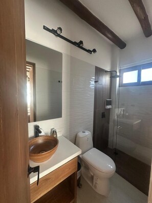 Une salle de bain moderne avec un grand miroir, un lavabo blanc, des toilettes et une douche à parois de verre.