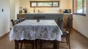 Ein Essbereich mit einem für vier Personen gedeckten Tisch, Holzstühlen, einer Chandelier und einer Küche im Hintergrund.