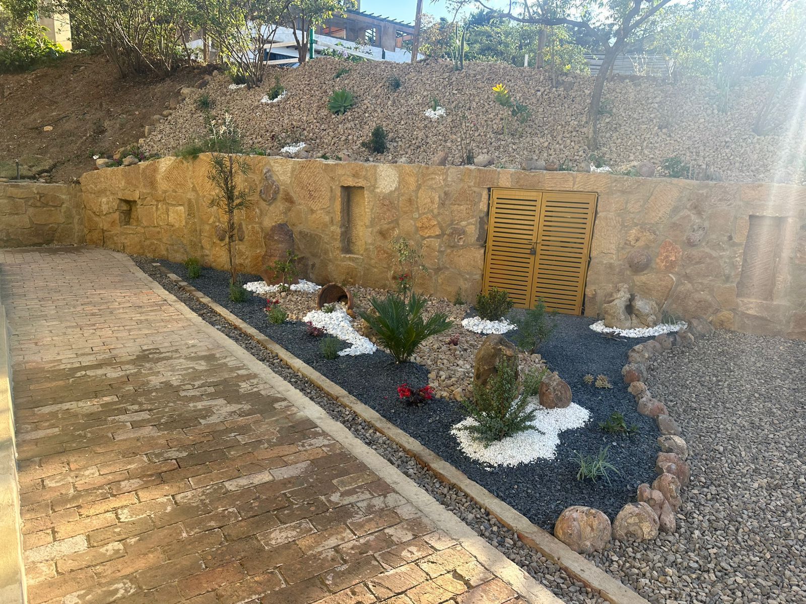 A landscaped garden with a stone wall, a wooden door, and a brick pathway.