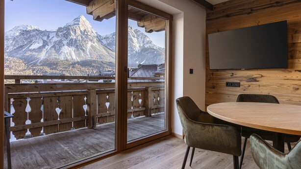 A room with a wooden balcony, a large window, and a flat-screen TV mounted on the wall. - Lavish Apartment With Sauna (Lermoos)