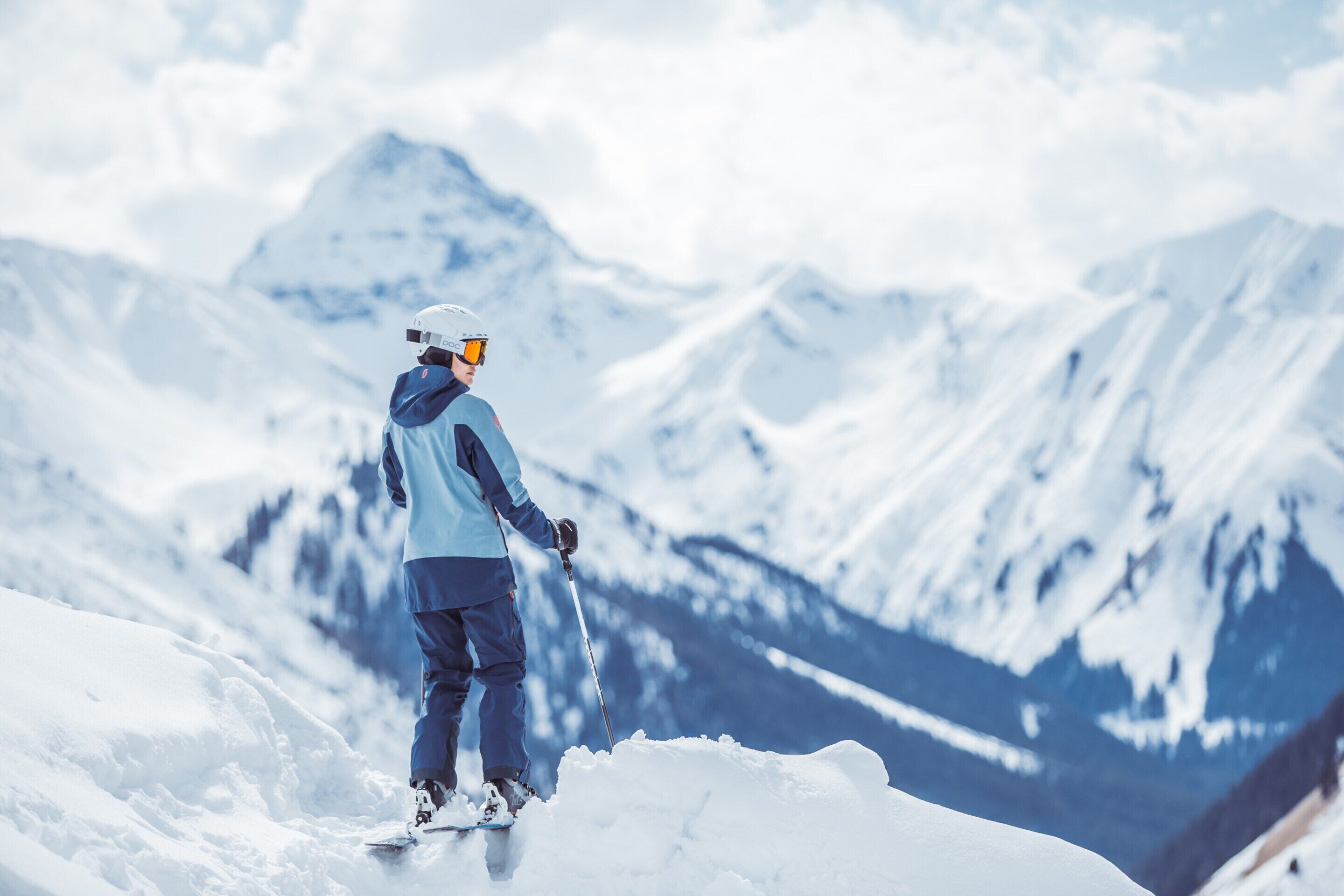 A person in winter gear standing on a snow-covered slope with a mountain in the background.
