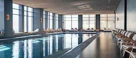 A large indoor swimming pool with multiple lounge chairs and sofas along the sides.