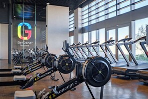 A gym with multiple cardio machines, including treadmills and stationary bikes, and a large window providing natural light.