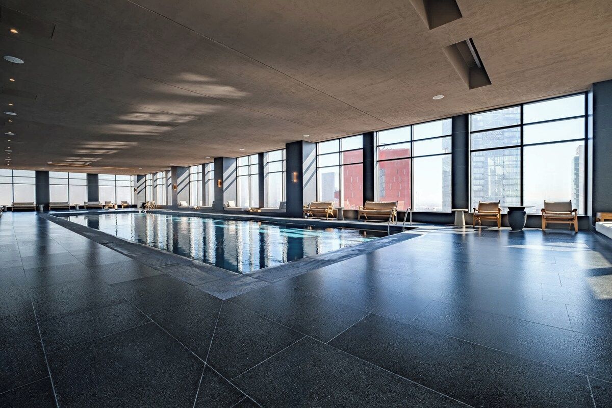 A spacious indoor swimming pool with clear views of the city skyline through large windows.