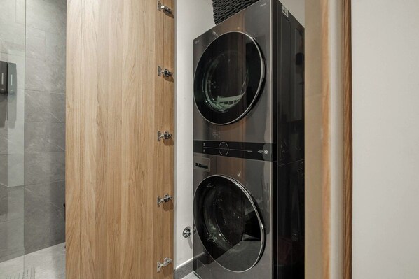 A modern laundry room with two front-loading washing machines, a wooden door, and a tiled floor.