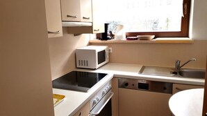 Una cocina compacta con microondas, estufa, lavaplatos y un ventanal que proporciona luz natural.