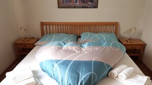 Una cama impecablemente tendida con una colcha azul y blanca estampada, dos almohadas y dos mesitas de noche con lámparas.
