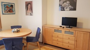 Una habitación con una mesa redonda, sillas azules, un armario de madera con un televisor y adornos en la pared.